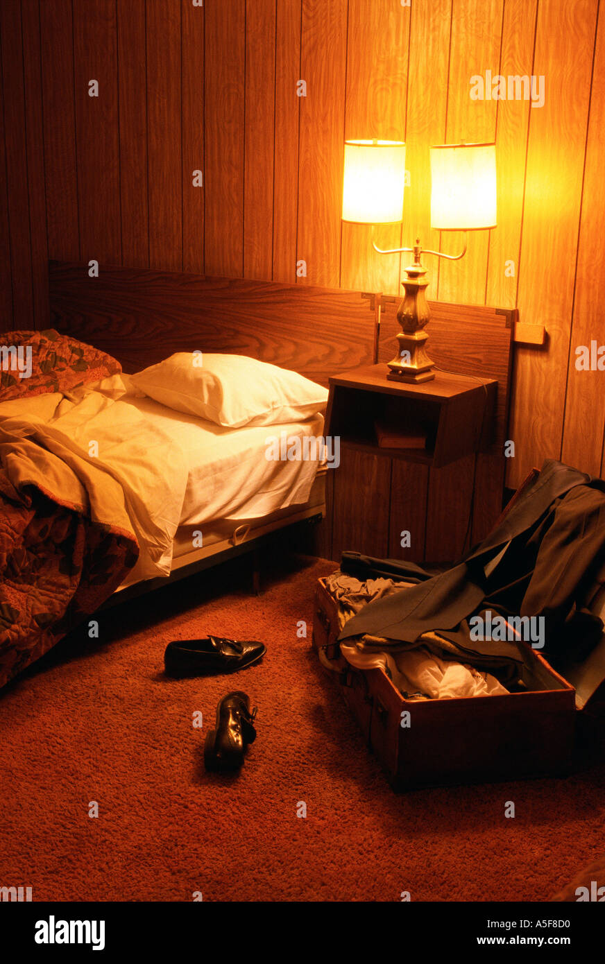 Evening view of motel room with unmade bed and unpacked suitcase on the floor Stock Photo