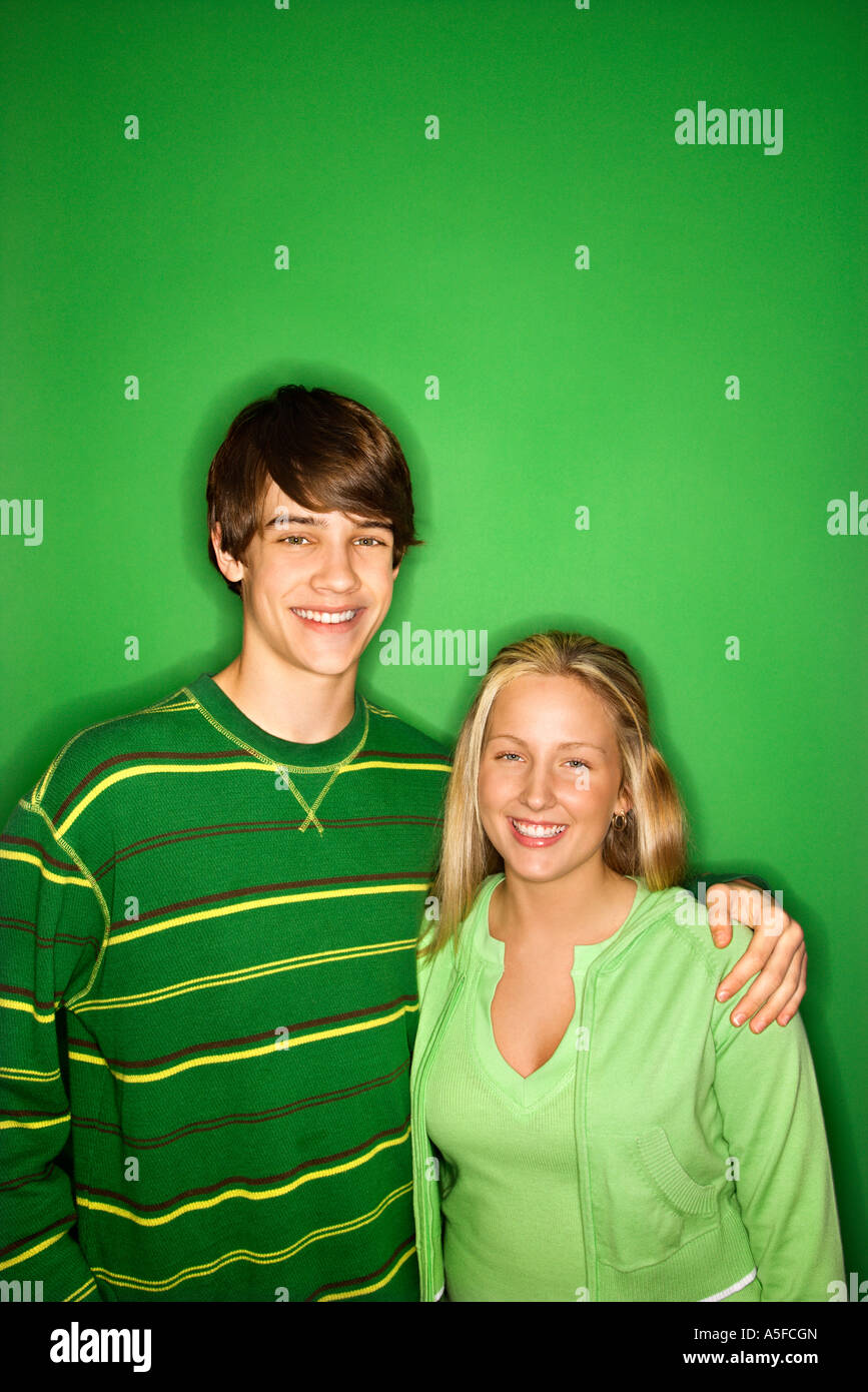 Portrait of Caucasian teen boy and girl standing against green ...