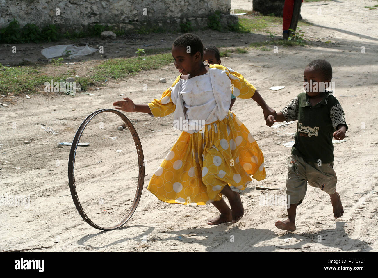 Children spinning a hoop on a dirt road, Stonetown, Zanzibar, Tanzania Stock Photo