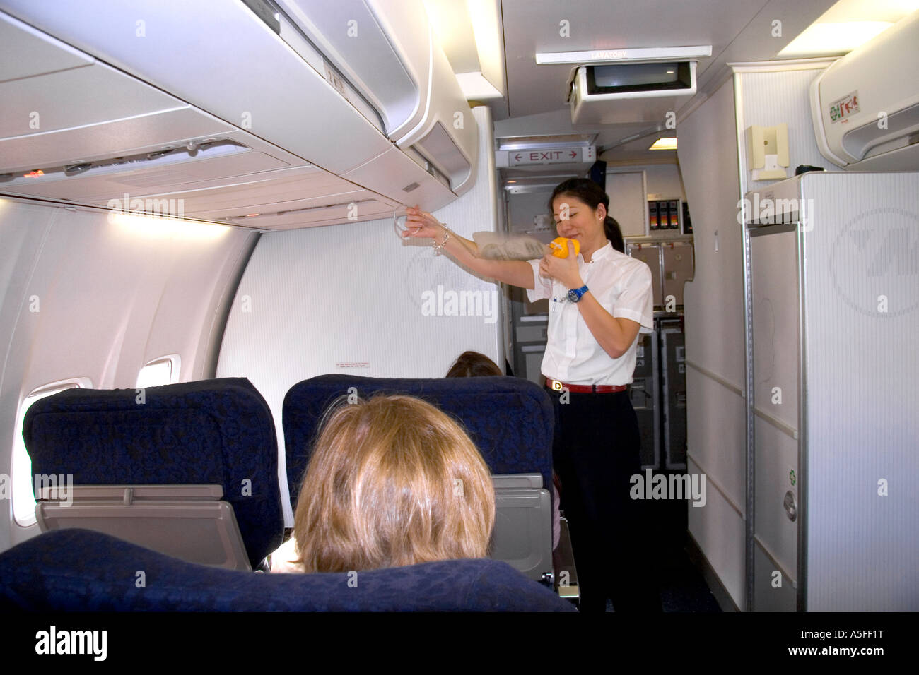 Flight attendent showing how to use an oxygen mask during the preflight safety intsructions Stock Photo