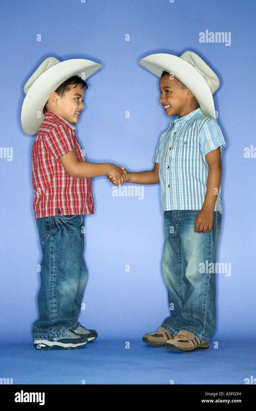 Hispanic and African American male child in cowboy hats shaking hands