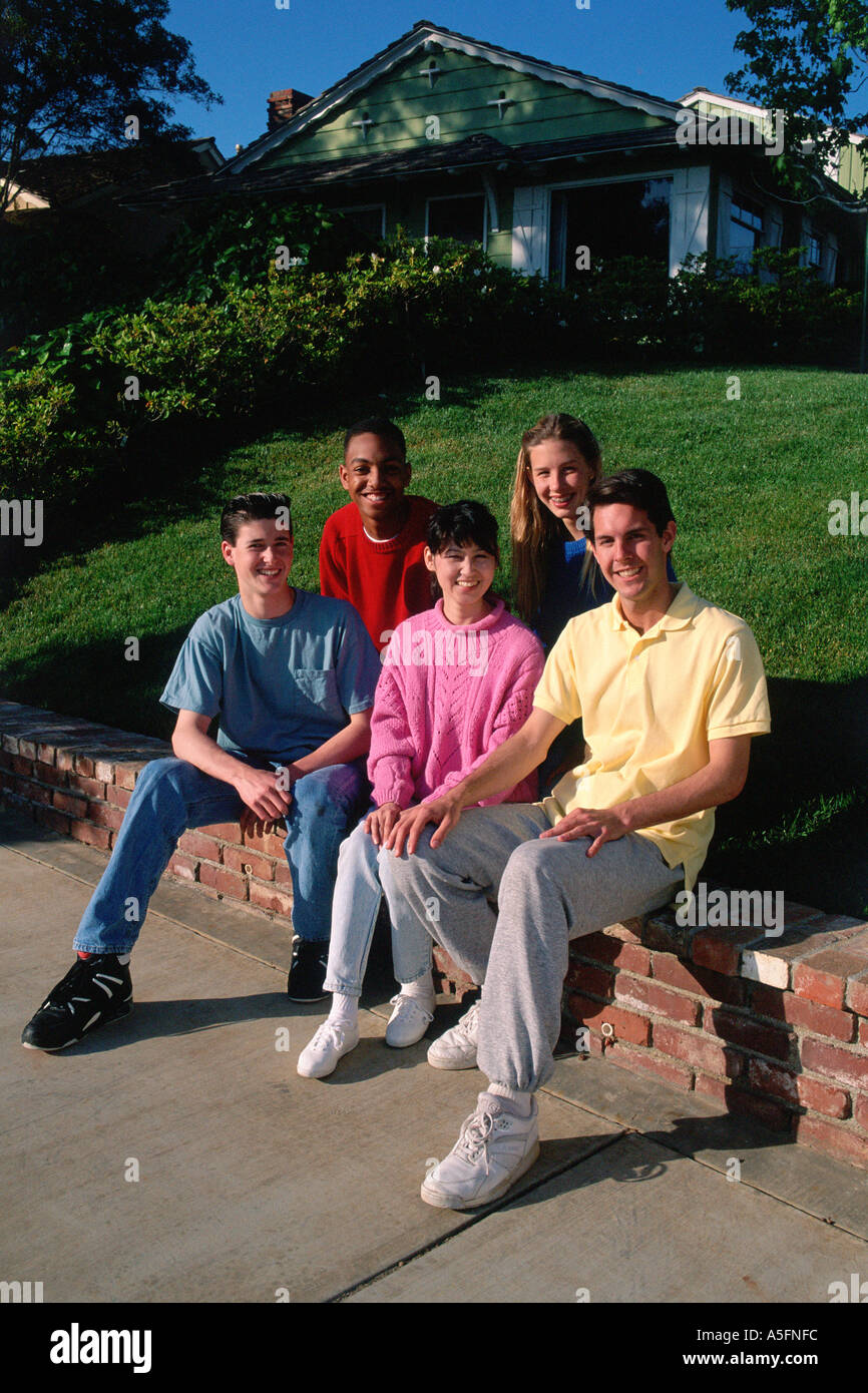 racially diverse, smiling, teenagers, friends sit on low wall near sidewalk, near home Stock Photo