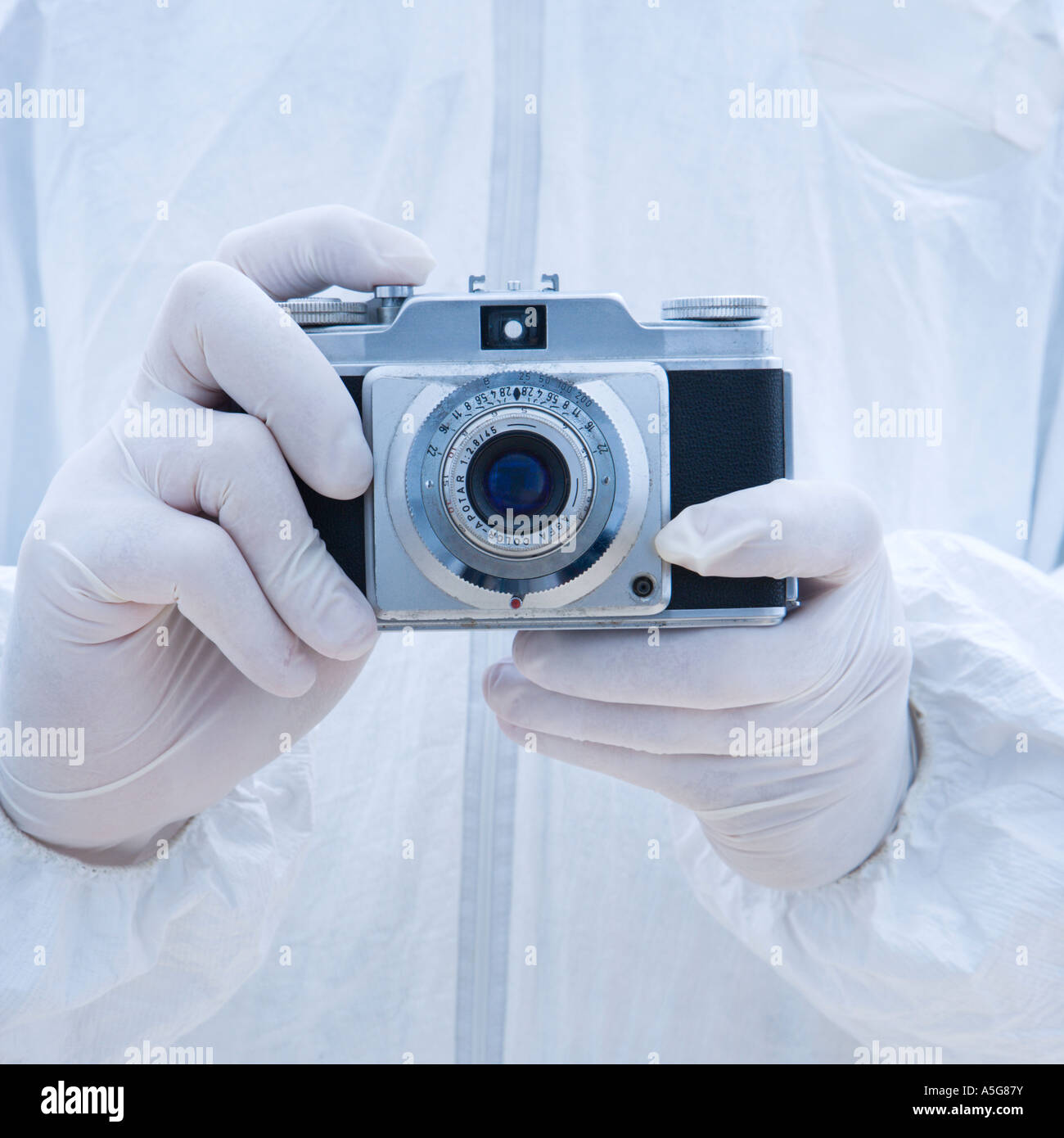 Man in biohazard suit holding antique camera with finger on shutter button Stock Photo