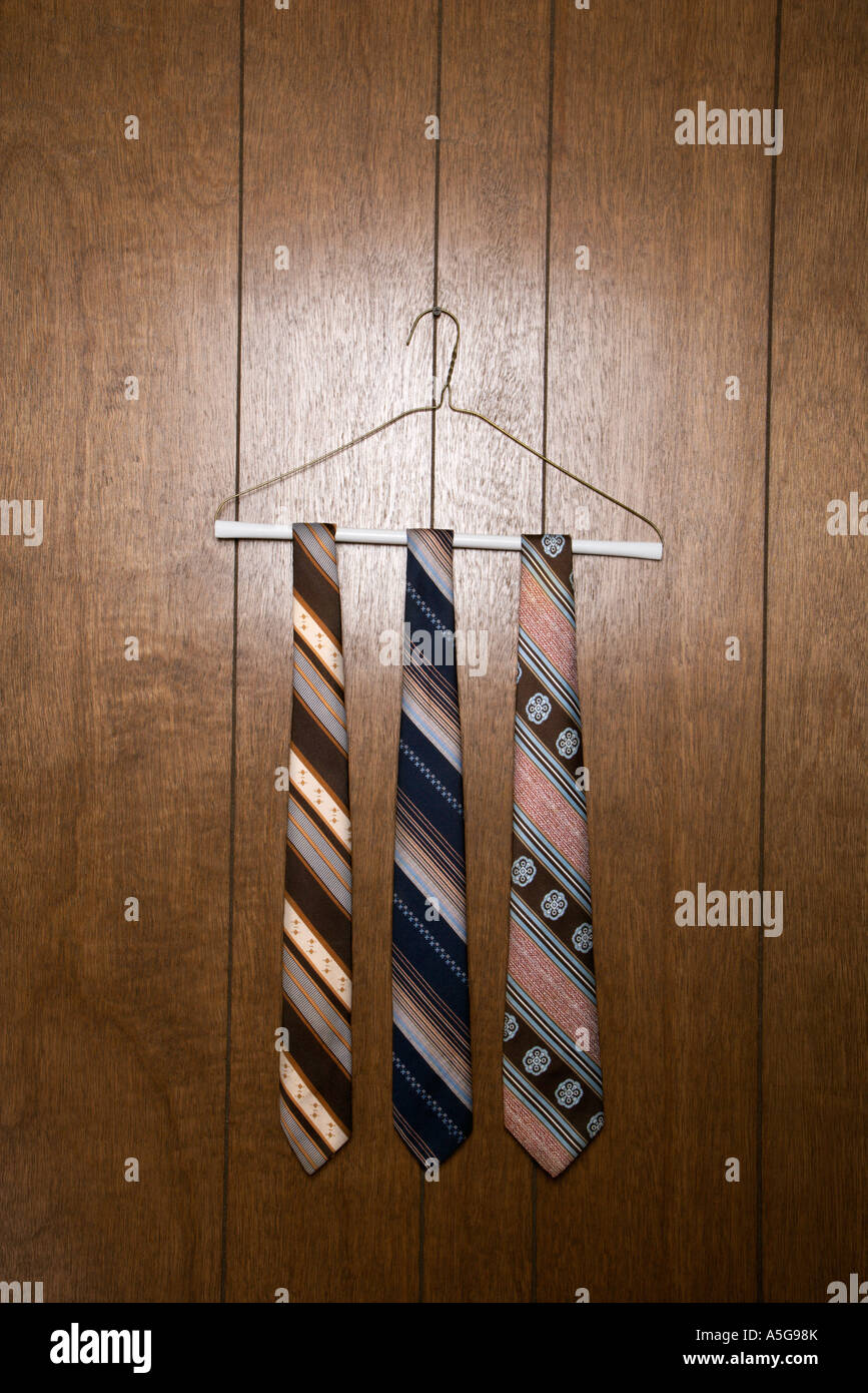 Three retro ties hanging on a wire hanger against wood paneling Stock Photo
