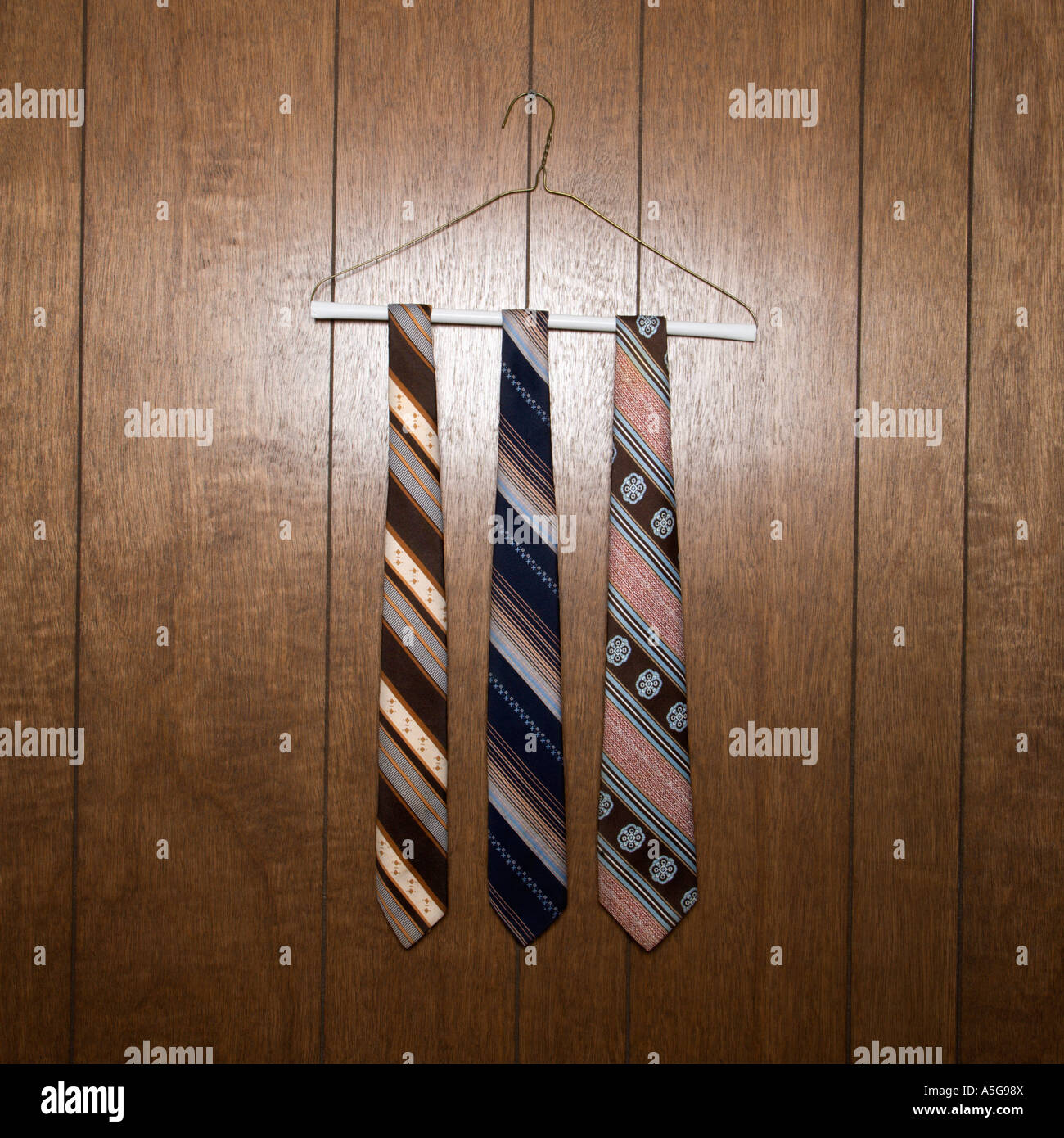 Three retro ties hanging on a wire hanger against wood paneling Stock Photo