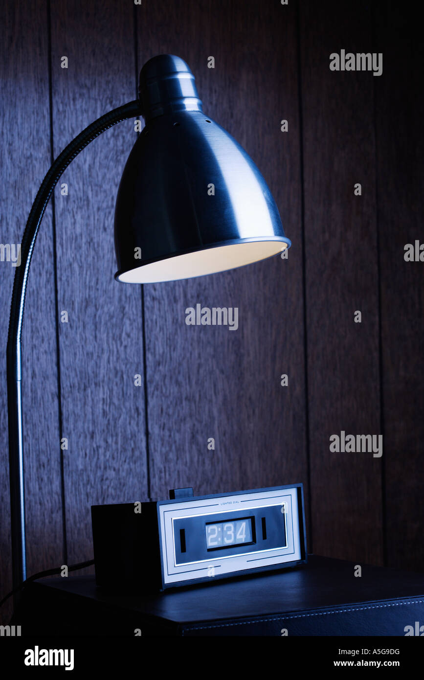 Dim desk lamp and retro clock against wood paneling at night Stock