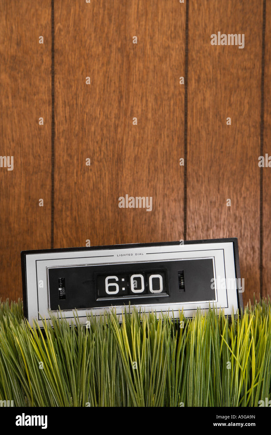 Studio shot of retro alarm clock placed in grass with wood paneling in ...