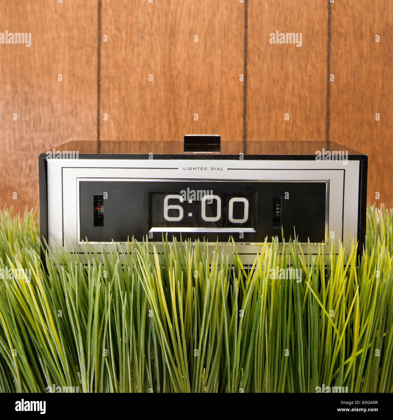 Studio shot of retro alarm clock placed in grass with wood paneling in ...