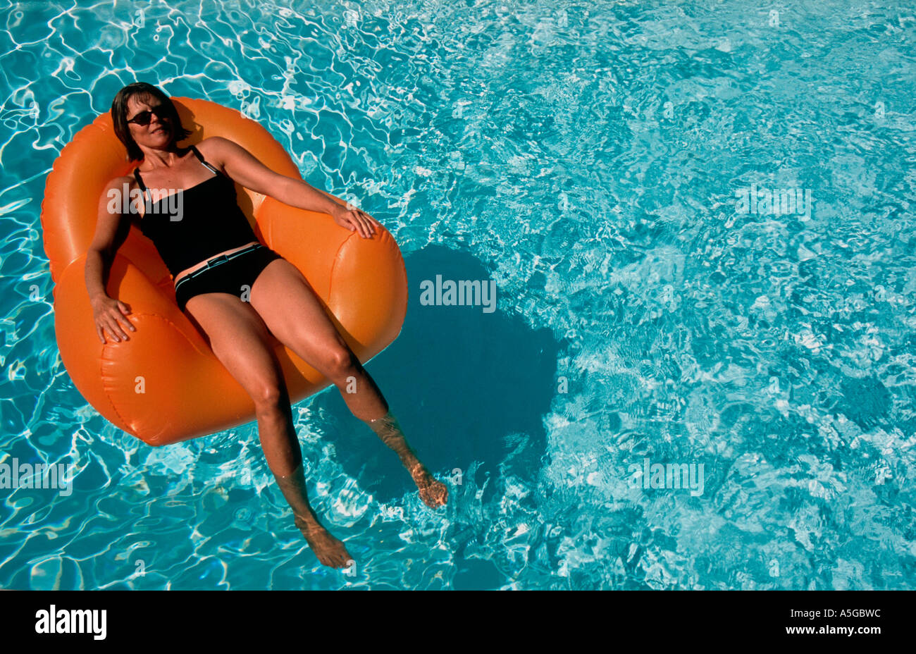 Woman 40 yrs reading on inflatable chair in swimming pool Kim Paumier Stock Photo