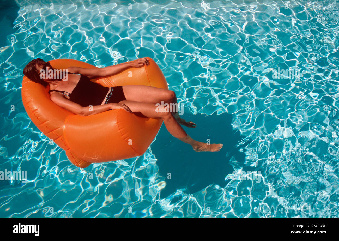 Woman 40 yrs reading on inflatable chair in swimming pool Kim Paumier Stock Photo