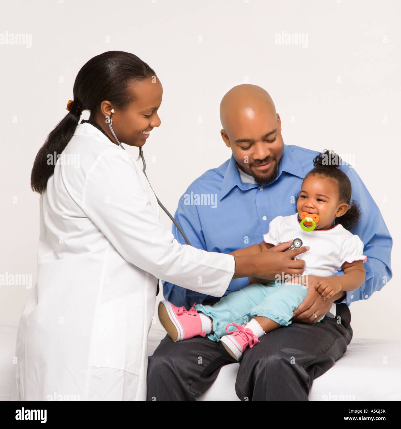 African American female pediatrician examining baby girl being held by ...