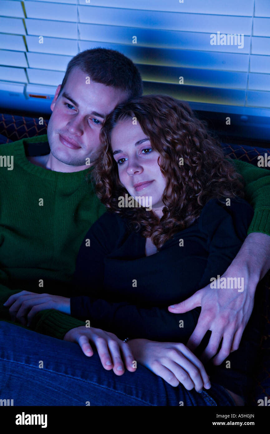 LIFESTYLE Twenties couple watch television sitting on sofa his arms around her Stock Photo