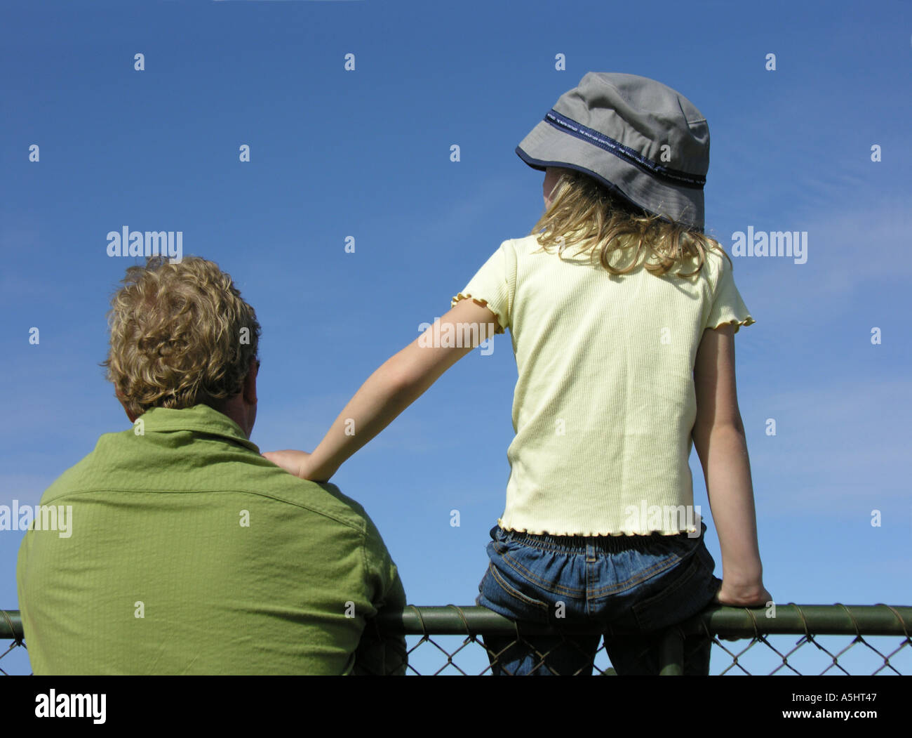 Father and little daughter leaning on shoulder sitting watching over fence Stock Photo