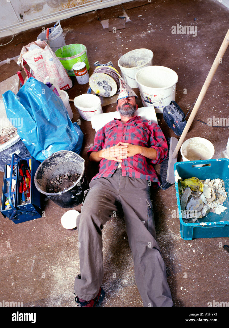 MR PR exhausted handyman do it yourselfer renovating a flat lying in middle of his tools and colour buckets Stock Photo