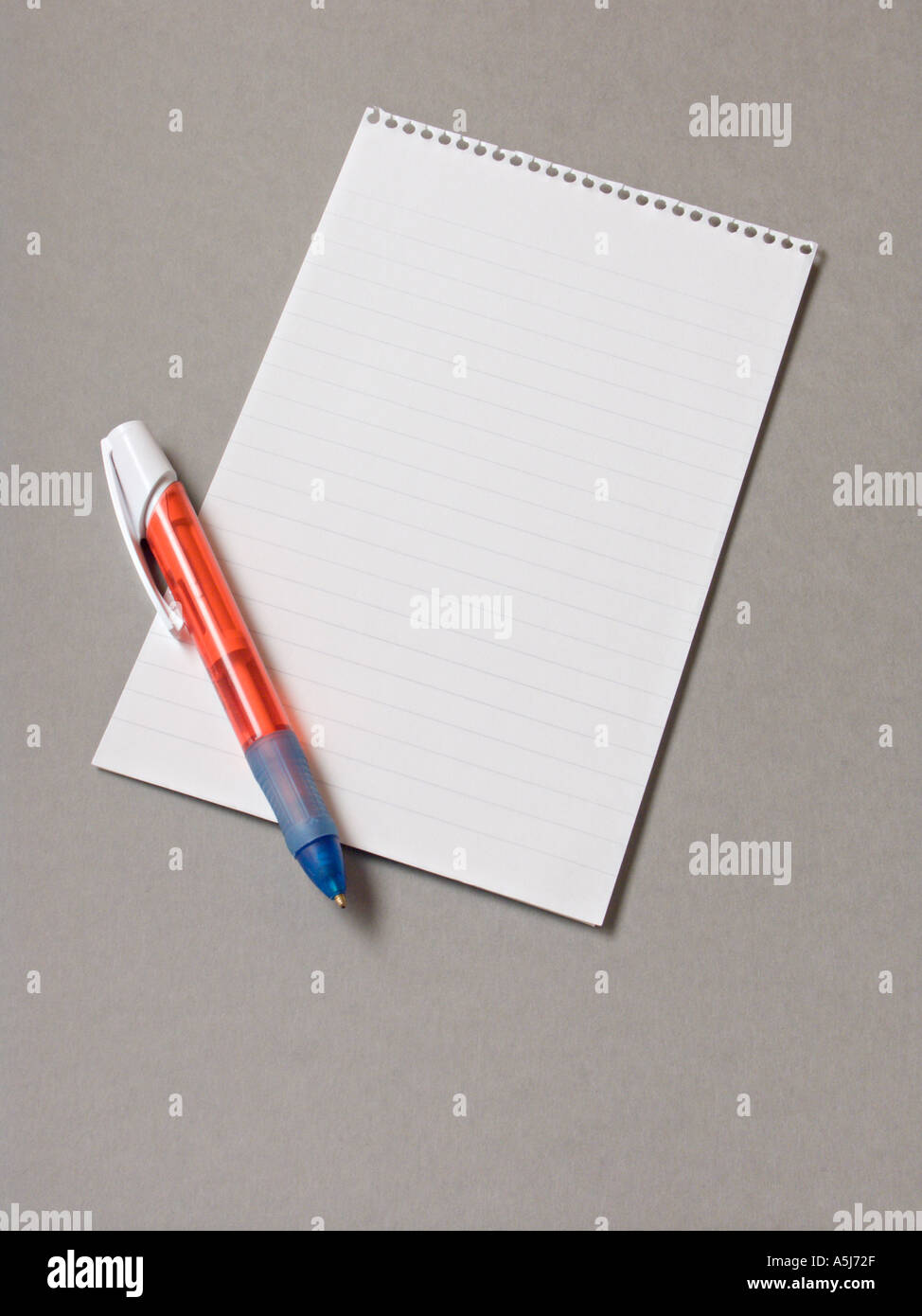 A spiral bound notepad with a red pen on a plain grey background Stock Photo