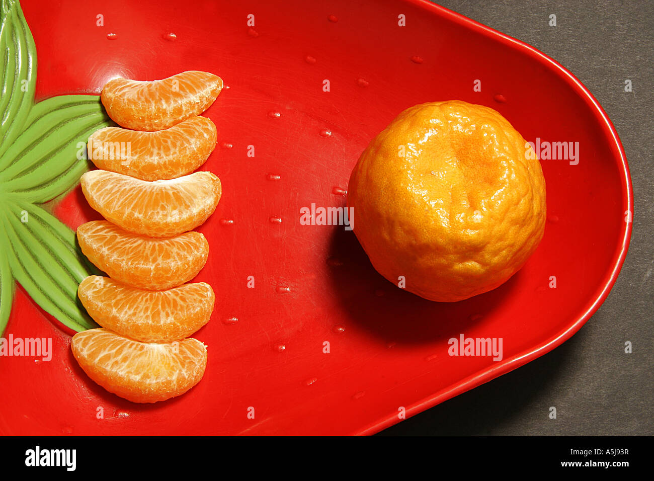 one full orange fruit and six pieces of orange in a red bowl Stock Photo