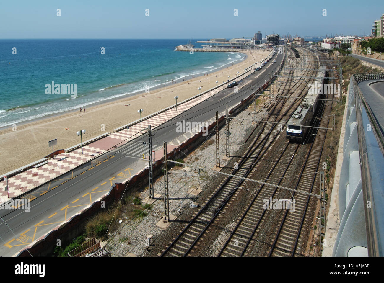 Urban landscape holiday beach road & railway tracks with Spanish train beside Mediterranean Sea coastline Tarragona Costa Daurada Catalonia Spain Stock Photo
