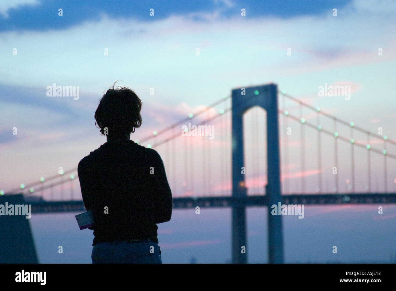 African American black female woman silhouetted standing on jetty rocks in front of Throgs Neck Bridge at sunset Stock Photo