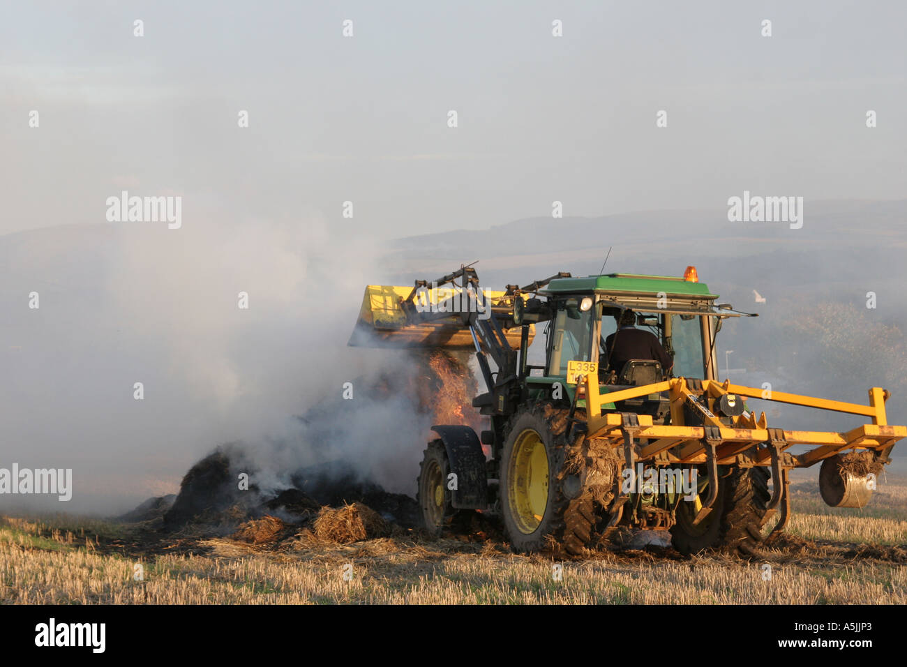 yellow tractor and burning stubble in field, East Lothian, UK Stock Photo