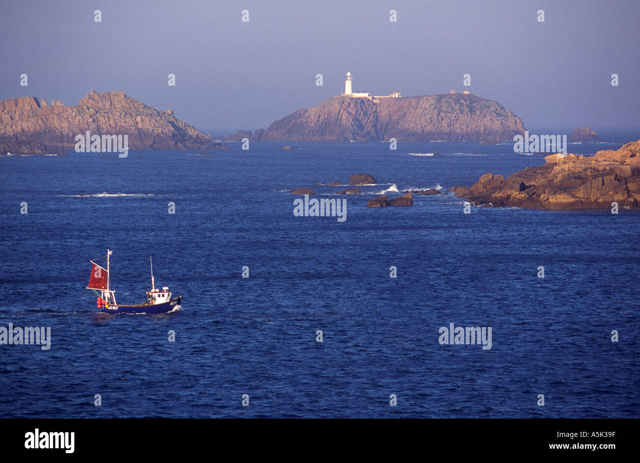 A fishing boat passes Round Island lighthouse Isles of Scilly Cornwall UK Stock Photo