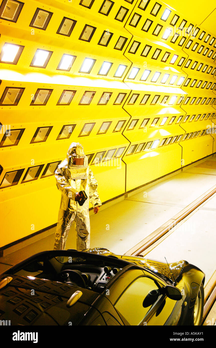 A Scientist in a Heat protection Suit is measuring the temperature fo a Car standing in the artificial climate wind channel and Stock Photo
