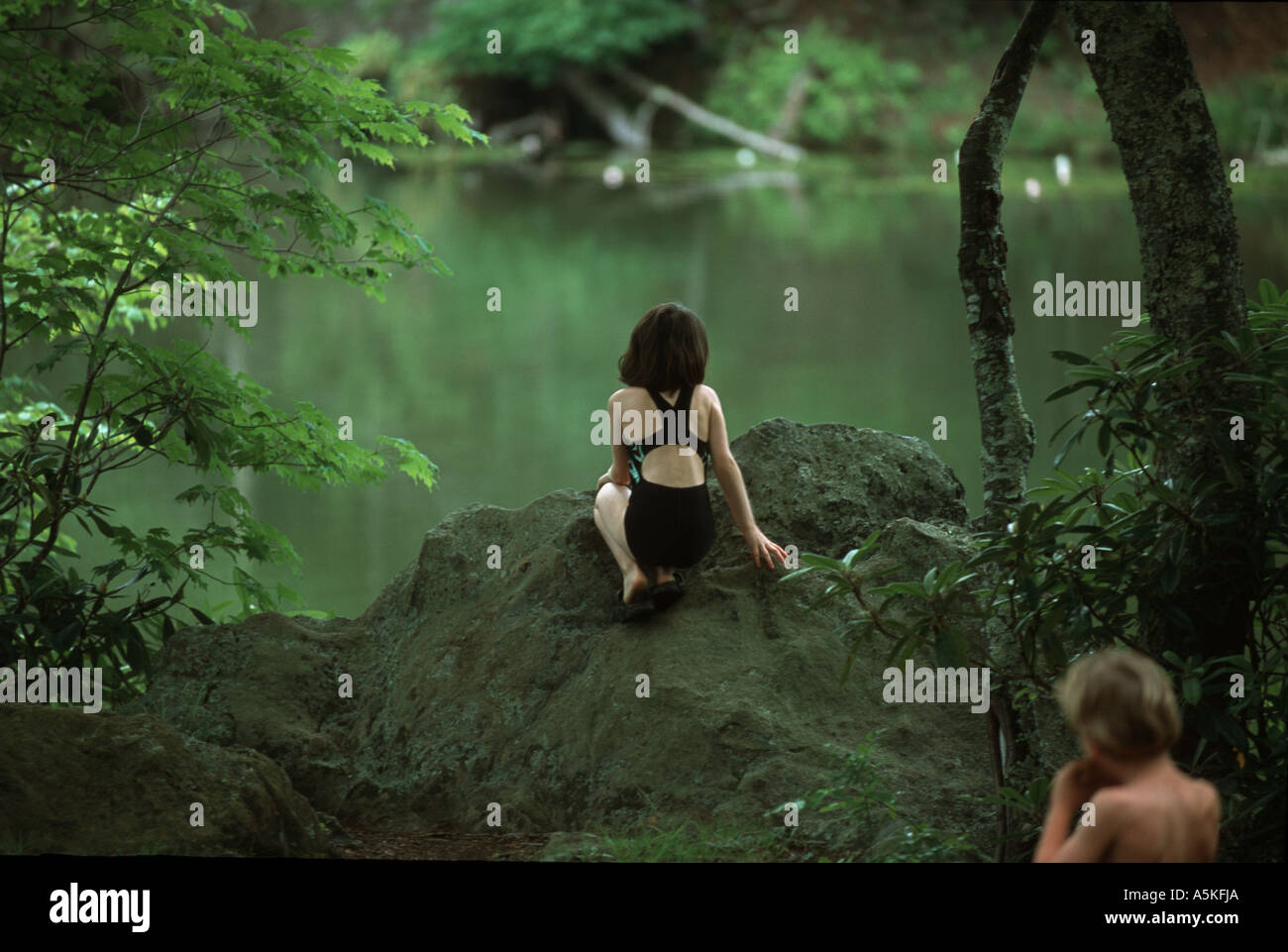 A Young Girl Wearing A Swimsuit Is Perched On The Ledge Of A Rock
