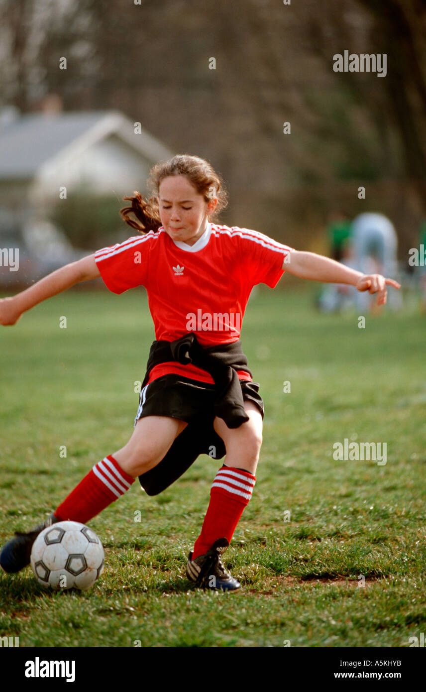 A young girl in a bright red soccer uniform concentrates on kicking the