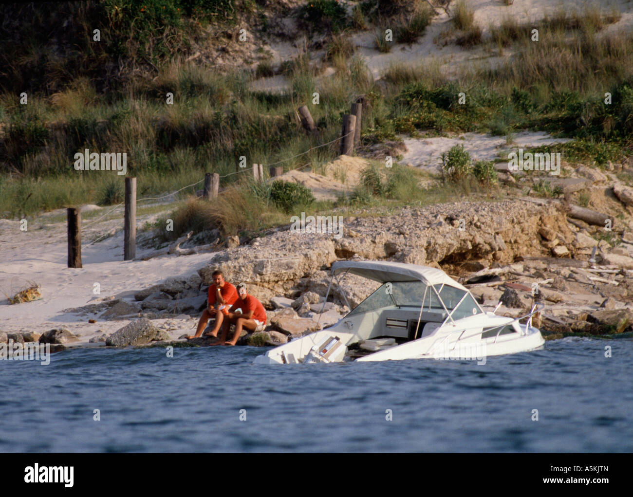 VA Chesapeake Beach Boat sinking near shore with its passengers resting safely on rocks Stock Photo