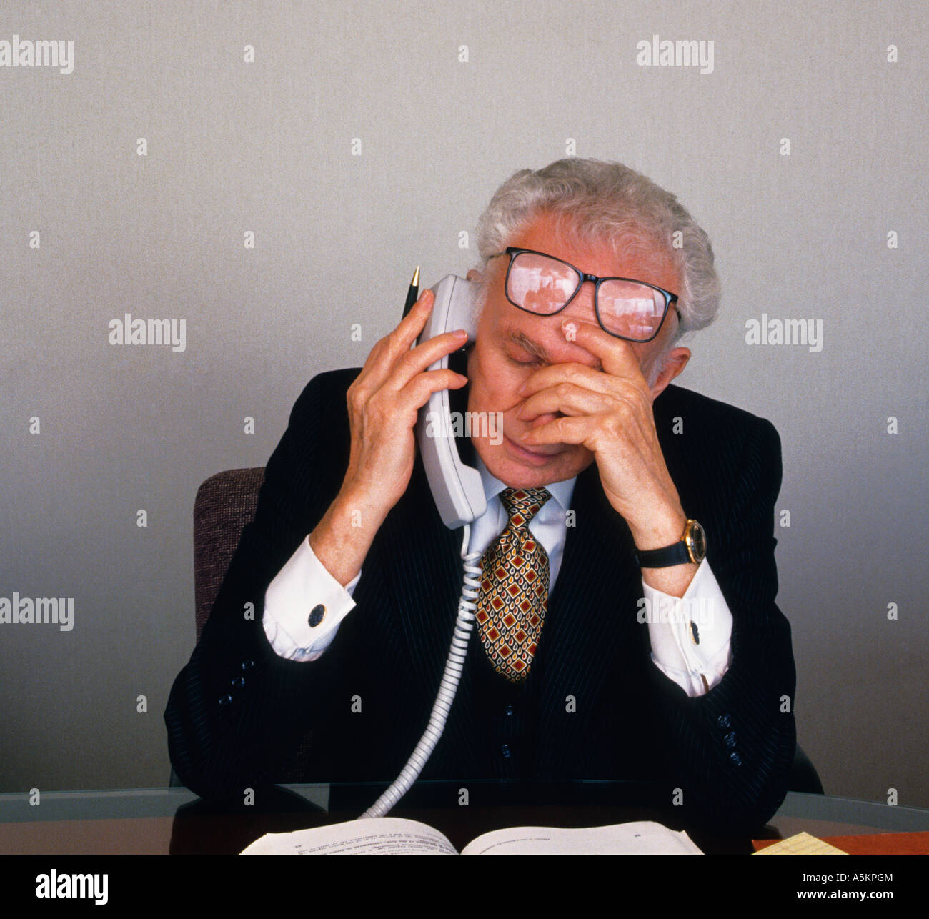 Elderly Man On the Phone in His Office Sitting At His Desk Concerned Tired and Overworked Stock Photo