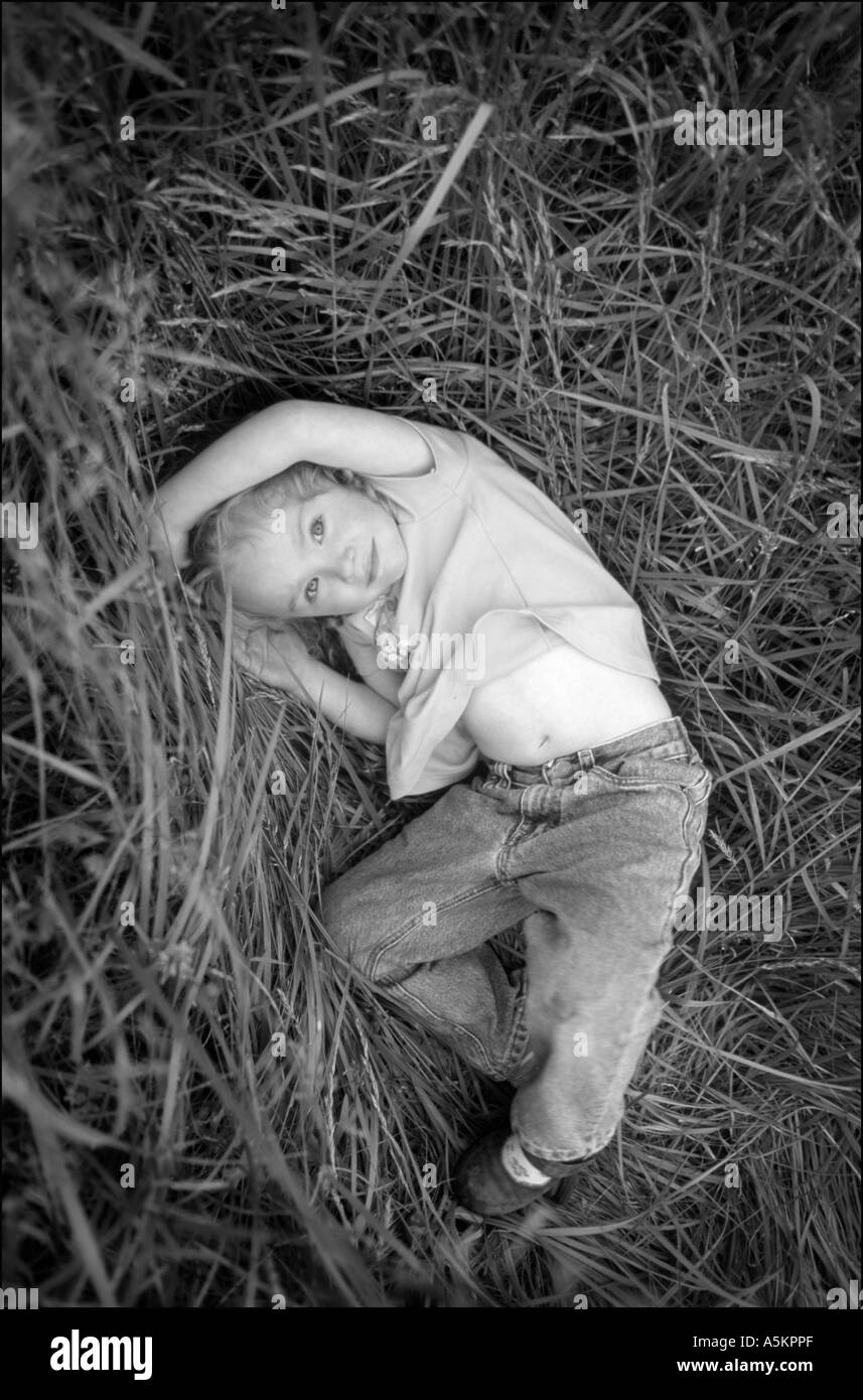 A beautiful young girl is lying down in a field of tall grass as she stares up innocently at the viewer in this black and white portrait Stock Photo