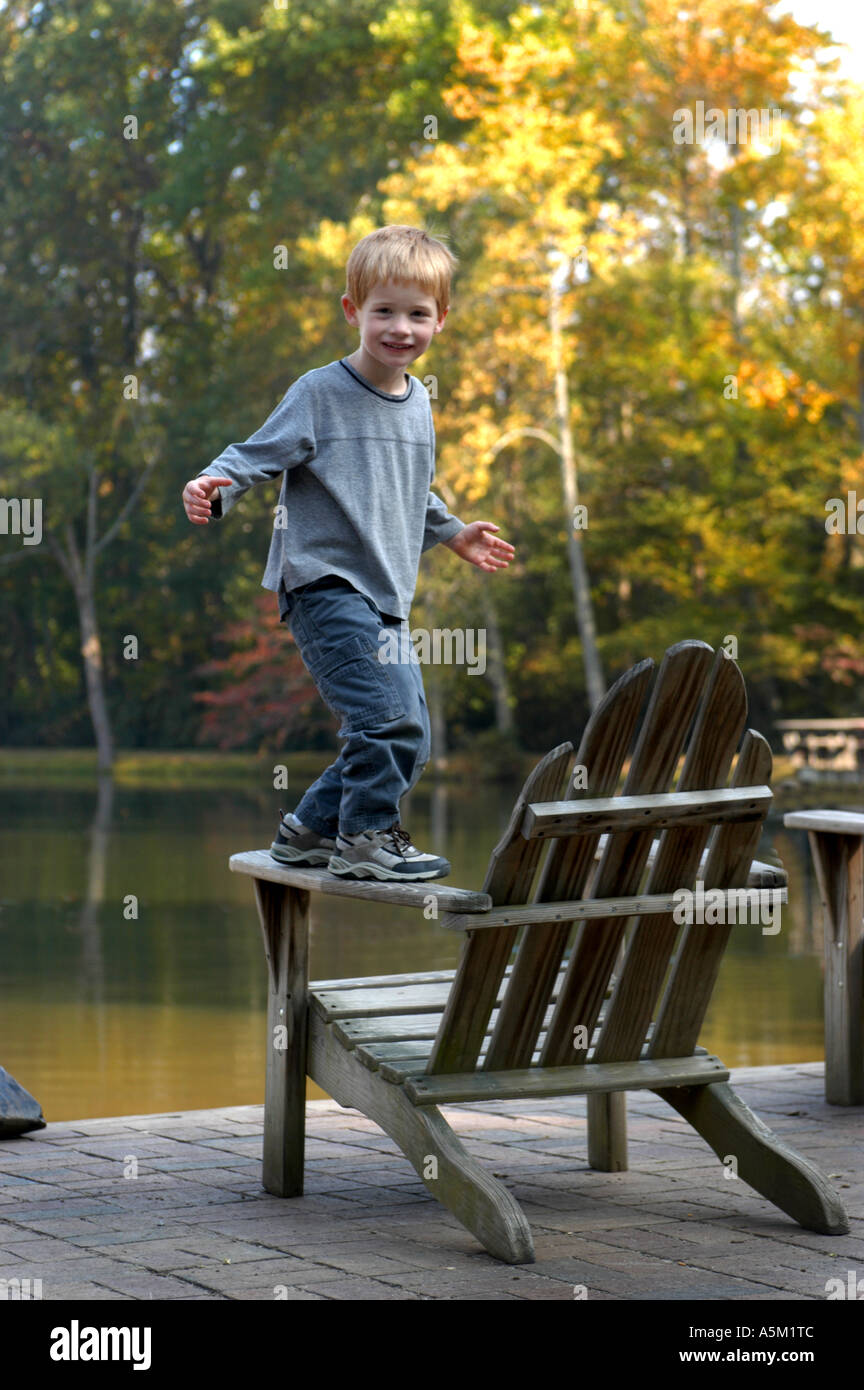 A Boy Balances On The Arm Of An Adirondack Chair Which Is By