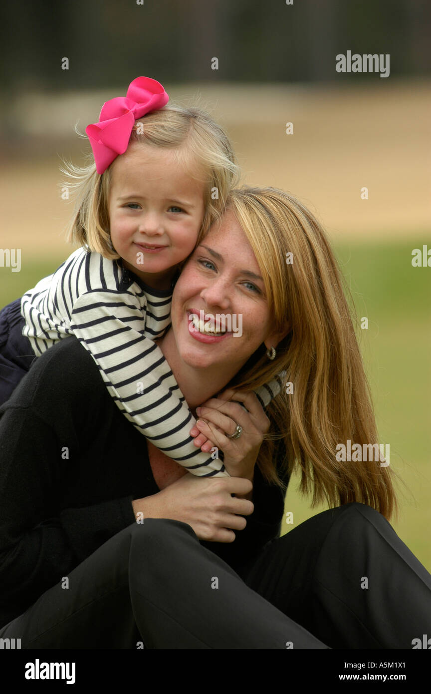 A young girl stands behind her mother and wraps her arms around her