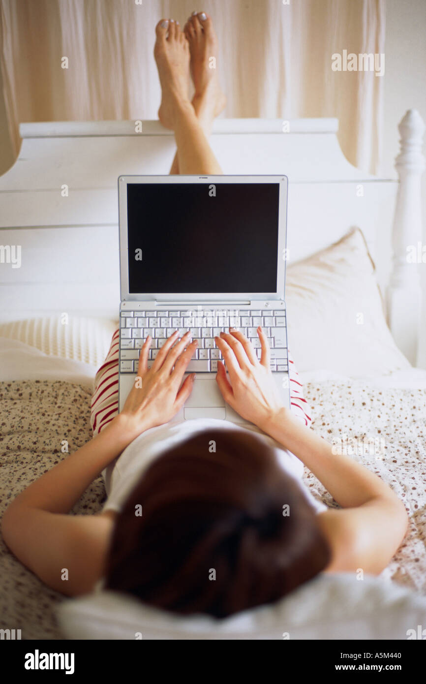 Woman lying on a bed with a laptop Stock Photo - Alamy