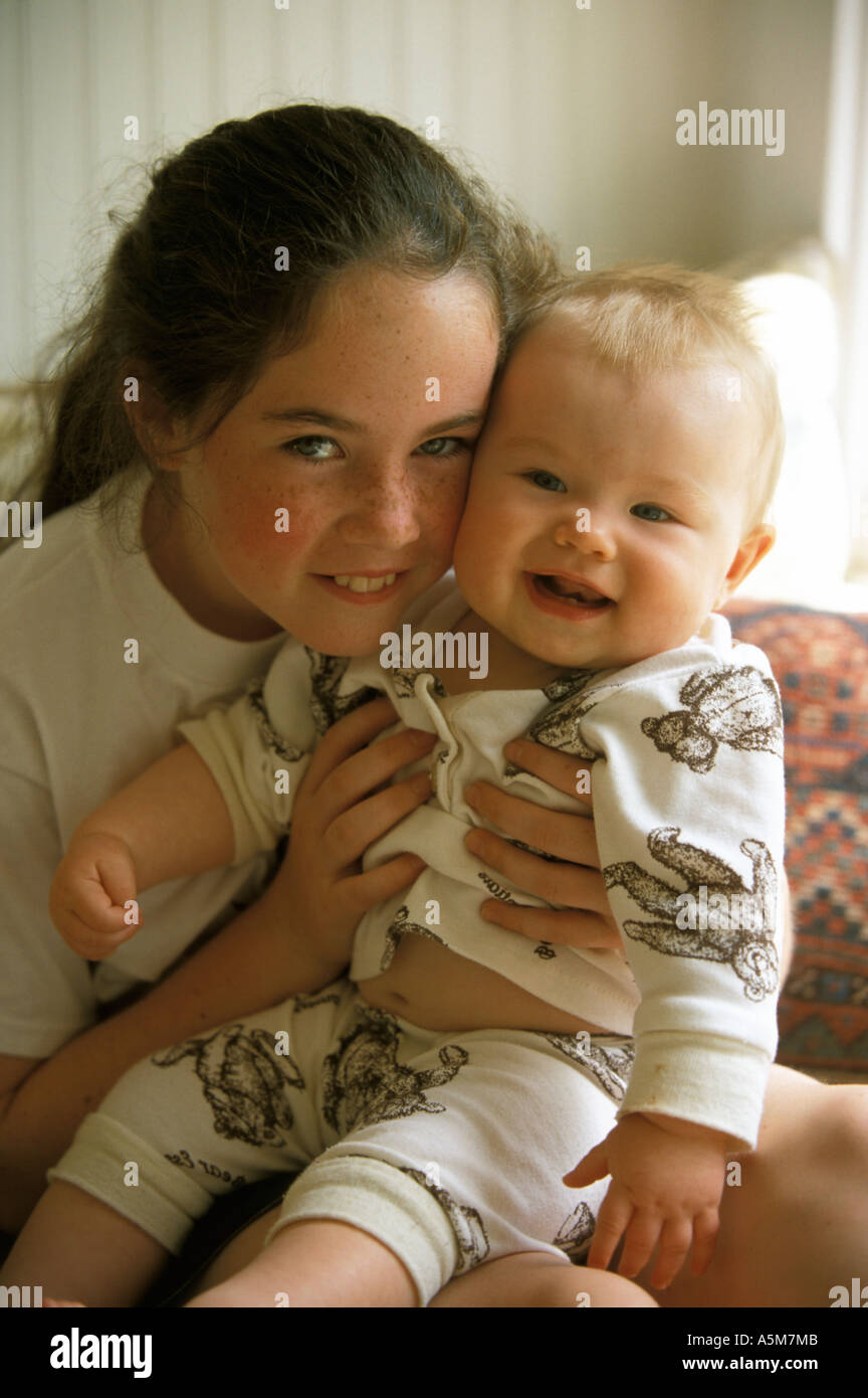 A ten year old girl is holding a six month old baby girl in her lap as they smile at the viewer