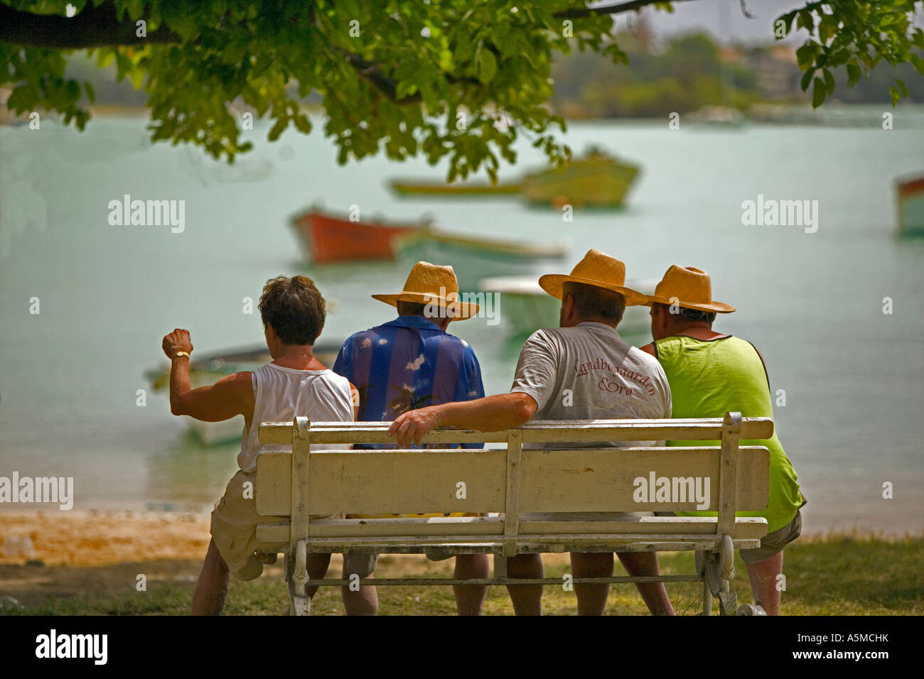 Hot day in Mauritius - Four men relaxing in the heat watching the fishing boats in the bay Stock Photo