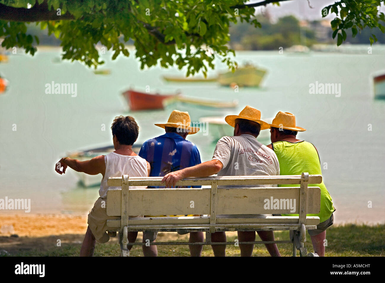 Hot day in Mauritius -  Four men relaxing in the heat watching the fishing boats in the bay Stock Photo