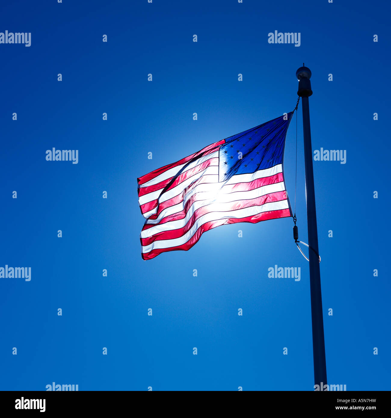 American flag on flagpole waving against blue sky with sun shining ...