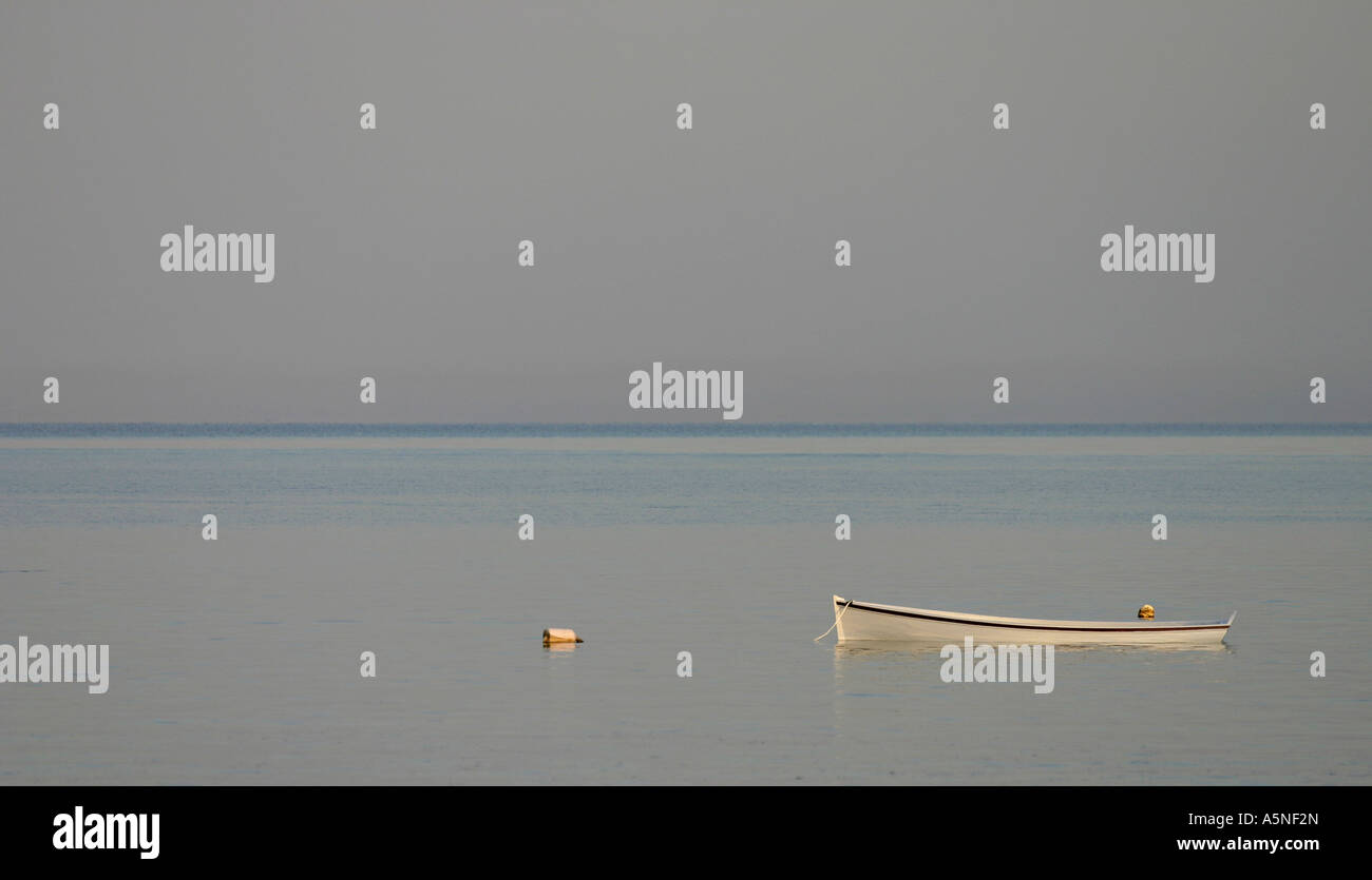 Dingy Sinking in a Misty Sea A small moored boat lying low and slowly sinking in a misty subtly coloured sea at sunset Stock Photo