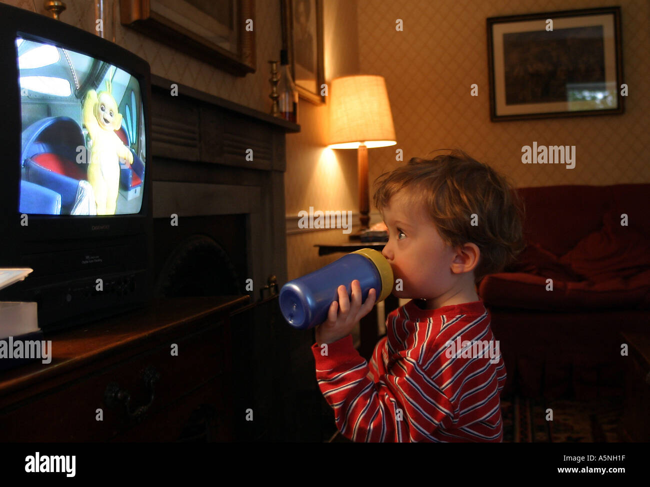 Lewis aged three watching Teletubbies on the television and drinking juice Stock Photo