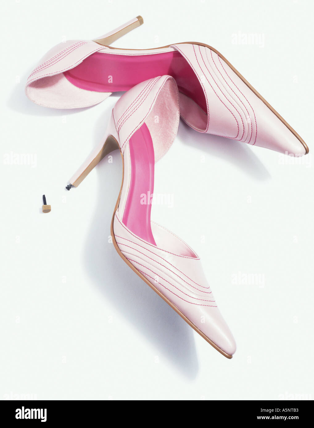 A pair of pink stiletto shoes one with the heel tip missing Stock Photo