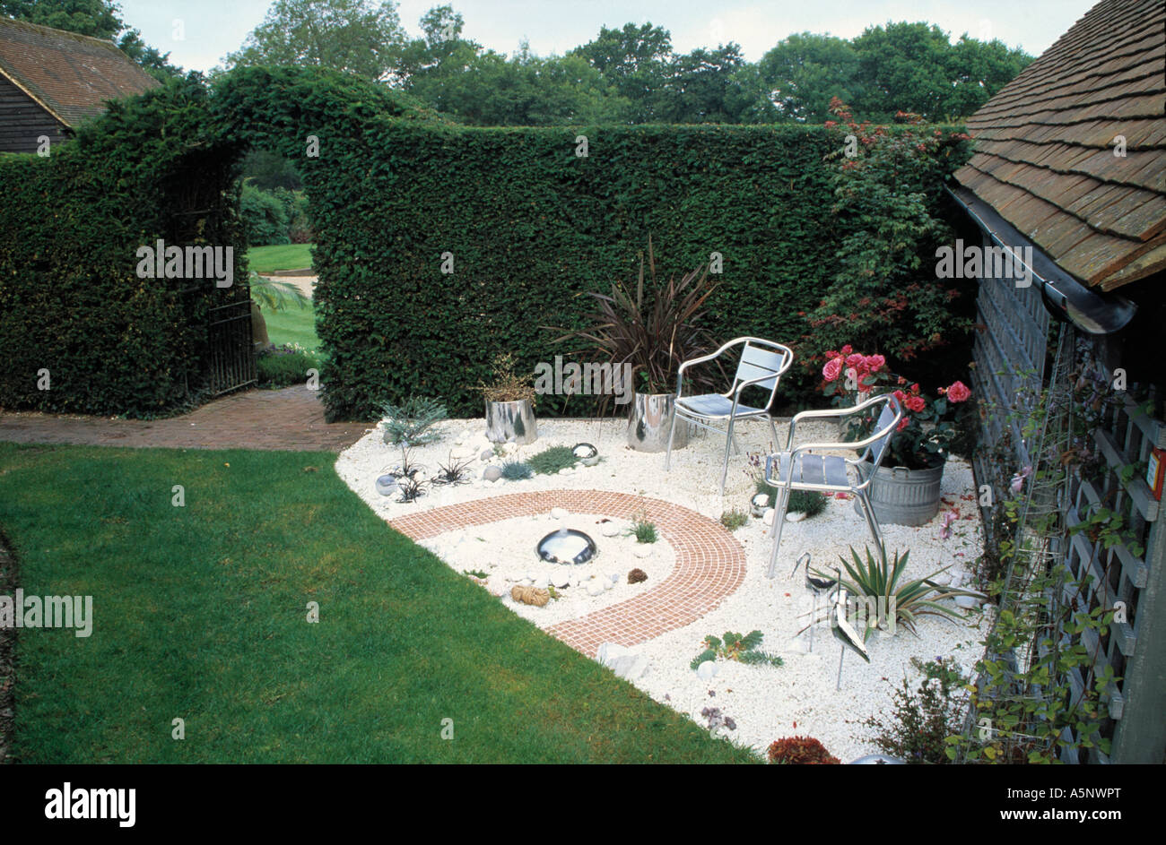 Metal chairs on gravel patio with brick path in corner of garden with