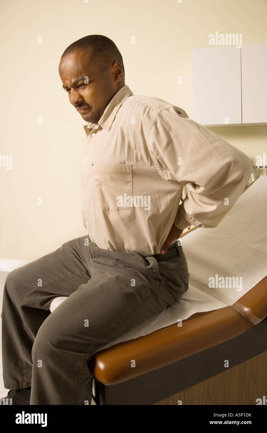 Man with back pain waits to see medical professional. Stock Photo