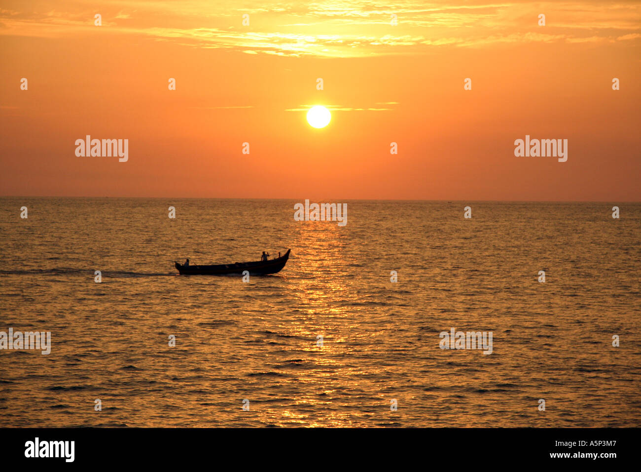 Beautiful sunset overlooking the arabian sea, Kovalam, Southern India, with traditional boat silhouetted in the distance Stock Photo
