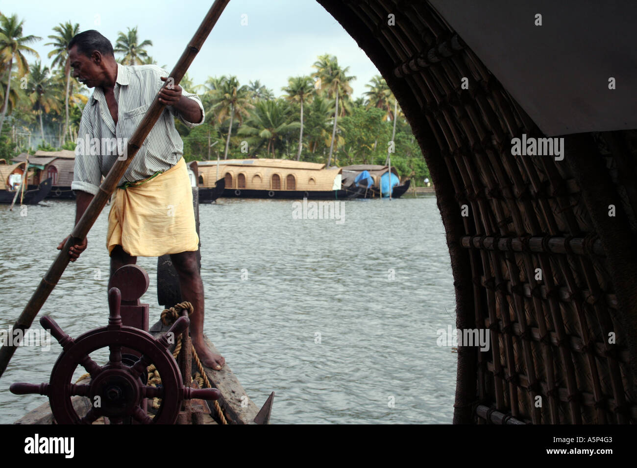 Man steering a houseboat on the backwaters of Kerala Stock Photo