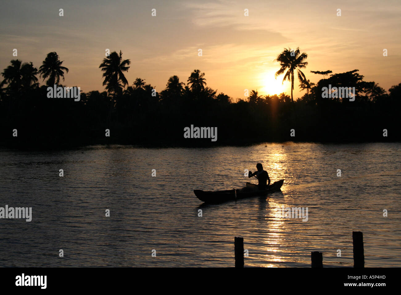 Stunning calm sunset from a moored houseboat on the backwaters of Kerala, with traditional canoe gliding past Stock Photo