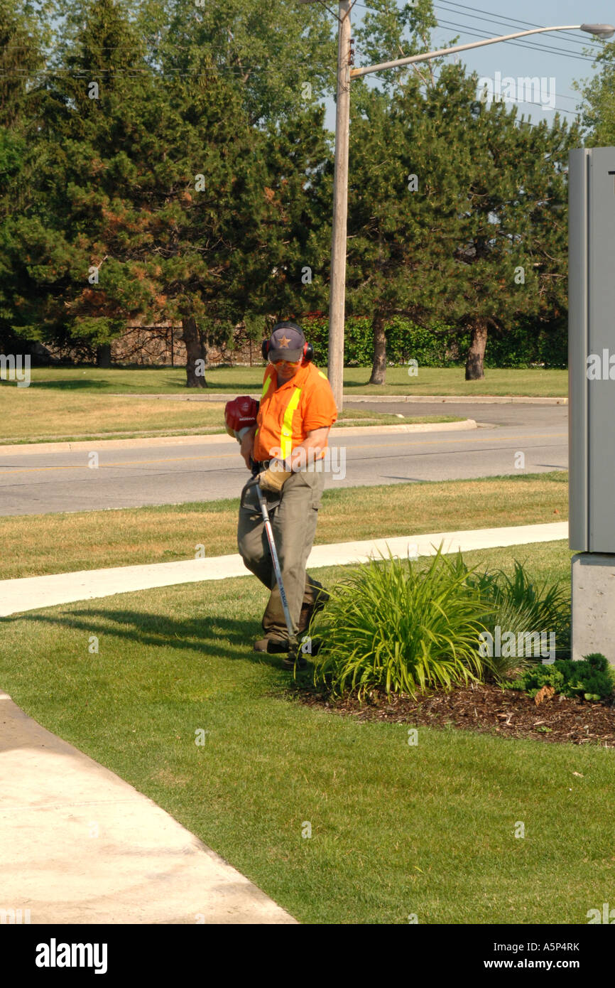 Professional Gardener using a weed-eater tidying up a border of a lawn around a commercial complex Stock Photo