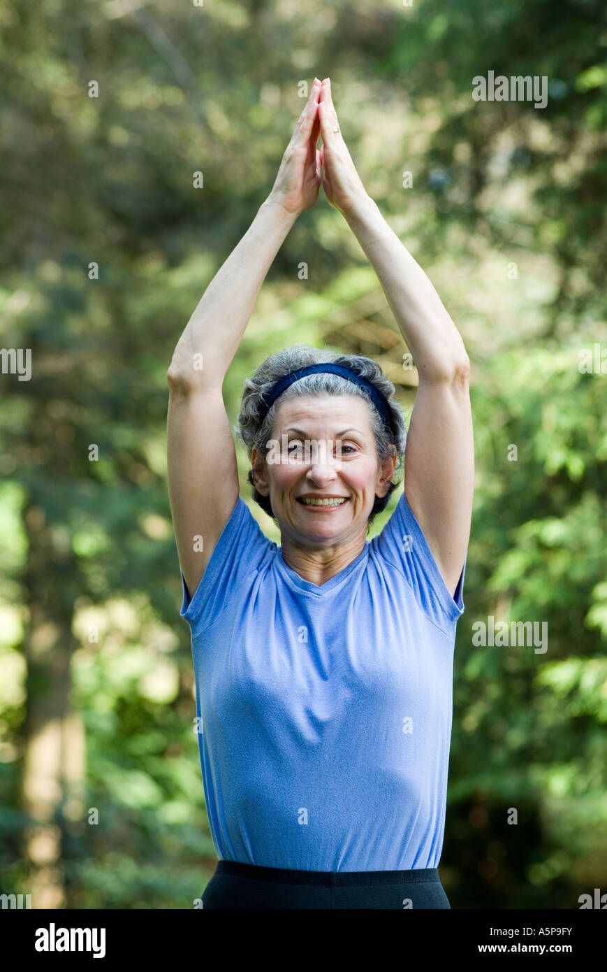 Older woman exercising outdoors, doing jumping jacks. Stock Photo