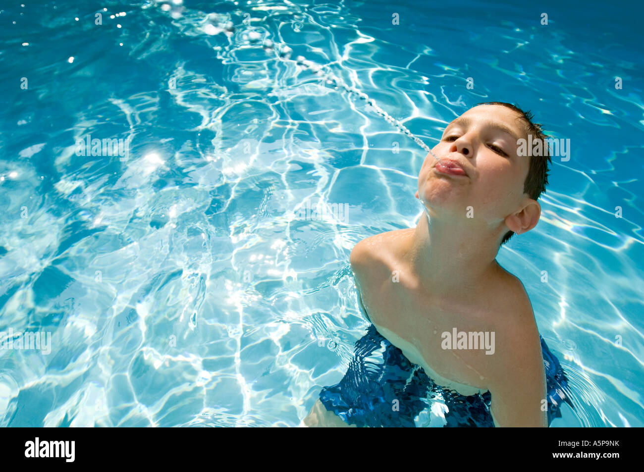 Boy squirting water in swimming pool. Stock Photo