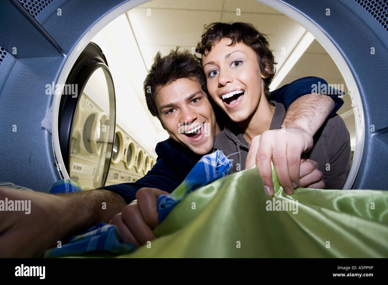 Young couple taking clothes out of dryer at Laundromat smiling Stock