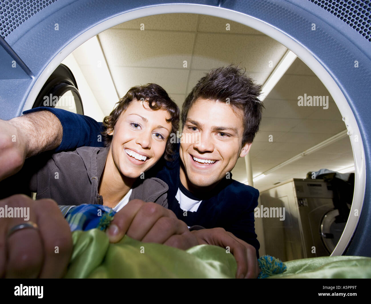 Young couple taking clothes out of dryer at Laundromat smiling Stock